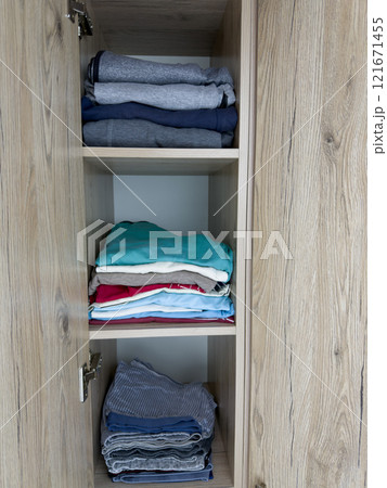 Vertical photo of closet shelves with home clean clothes in wooden closet with an open door, storing clean clothes at home on closet shelves, stacked clean clothes Vertical photo of closet shelves with home clean clothes in wooden closet with an open door, storing clean clothes at home on closet shelves, stacked clean clothes 121671455