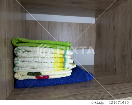 Stack of multi colored towels on wooden shelf inside large closet for clothes and things, storage space in apartment, shelf with towels for body hygiene at home Stack of multi colored towels on wooden shelf inside large closet for clothes and things, storage space in apartment, shelf with towels for body hygiene at home 121671459