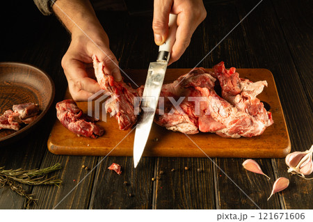 Hands skillfully prepare raw beef meat on a wooden cutting board, showcasing the art of butchery. Nearby, garlic and herbs hint at flavorful culinary creations waiting to be made 121671606
