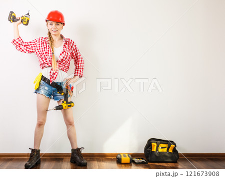 Woman wearing helmet, toolbelt about to drill wall 121673908