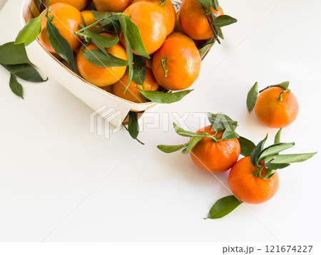 Fresh ripe mandarins with green leaves in wooden basket on white background Fresh ripe mandarins with green leaves in wooden basket on white background 121674227