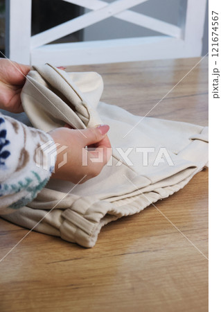 A woman is examining classic beige trousers. She is demonstrating the design elements. Oblique Angle.  121674567