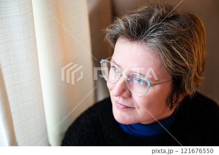 Window portrait of a 38 yo white woman at home in Brussels Old Town, Belgium 121676550