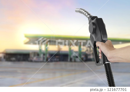 Holding a fuel nozzle against with gas station blurred background Holding a fuel nozzle against with gas station blurred background 121677701