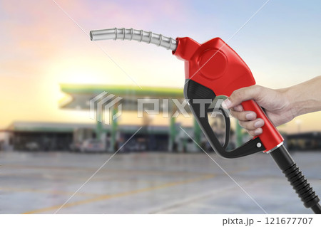 Holding a fuel nozzle against with gas station blurred background 121677707