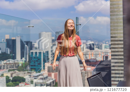 Female tourist or businesswoman standing on a skyscraper rooftop with a panoramic view of Mexico City. Travel or international business in Mexico concept Female tourist or businesswoman standing on a skyscraper rooftop with a panoramic view of Mexico City. Travel or international business in Mexico concept 121677720