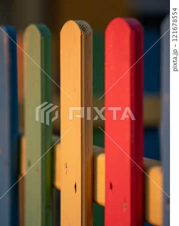 The colorful painted wooden boards on the fence around a playground are illuminated by the rays of the setting sun. Pula, Croatia - January 3, 2025 121678554