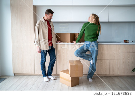 Happy woman dreaming looks stands with man near cardboard boxes in kitchen while moving in new home Happy woman dreaming looks stands with man near cardboard boxes in kitchen while moving in new home 121678658
