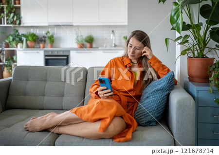Calm focused woman use cellphone sitting on sofa making online purchases or order delivery. Calm focused woman use cellphone sitting on sofa making online purchases or order delivery. 121678714