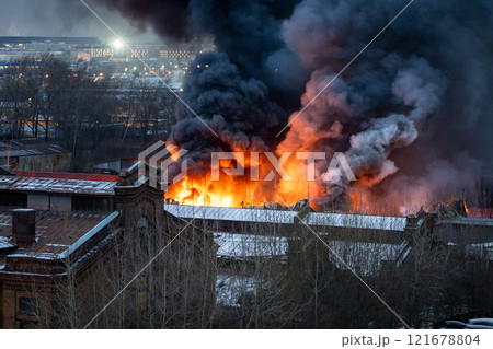 Burning factory building with orange flames, sparks and thick toxic smoke from heavy fire in morning 121678804