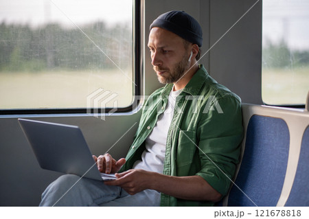 Focused tech savvy businessman type on laptop, wearing earphones while traveling by train to work Focused tech savvy businessman type on laptop, wearing earphones while traveling by train to work 121678818