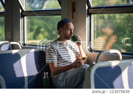 Calm man sip tea from thermos, chatting on smartphone in train car in morning. Male travel pause Calm man sip tea from thermos, chatting on smartphone in train car in morning. Male travel pause 121678830