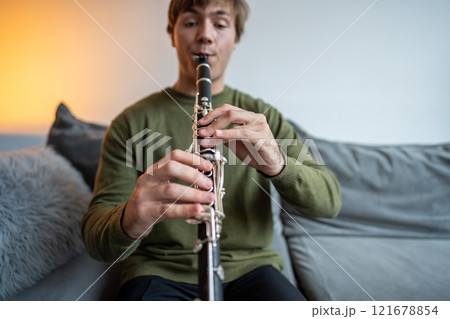 Clarinet player. Clarinetist hands playing flute woodwind music instrument at home. Guy plays oboe 121678854