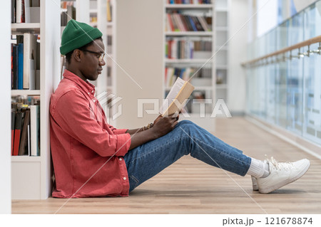 Concentrated African American student man with book spending free time in library, enjoying reading. Concentrated African American student man with book spending free time in library, enjoying reading. 121678874
