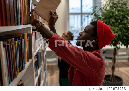 Concentrated African American student man picking books for preparing for exam in university library Concentrated African American student man picking books for preparing for exam in university library 121678958