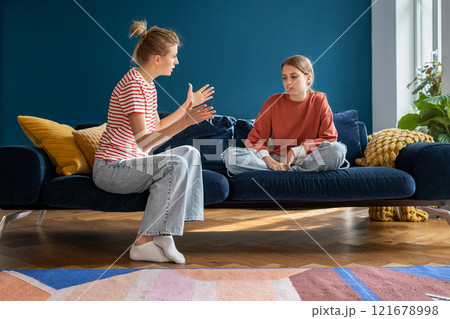 Upset annoyed parent mom talking arguing with teen girl daughter sitting on couch at home. 121678998