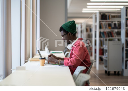 Focused African American student guy sitting at desk with laptop using online library database Focused African American student guy sitting at desk with laptop using online library database 121679048