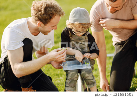 Dad, his friend and his child boy spend time outdoors together. Curly toddler boy wearing a khaki overall. Boy listening how to fish properly. 121681505
