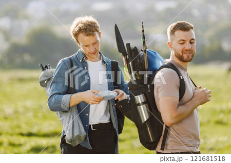 Friends is ready to fishing. Man holding a fishing equipment and other helps him. One man wearing rose t-shirt and other blue shirt. Friends is ready to fishing. Man holding a fishing equipment and other helps him. One man wearing rose t-shirt and other blue shirt. 121681518