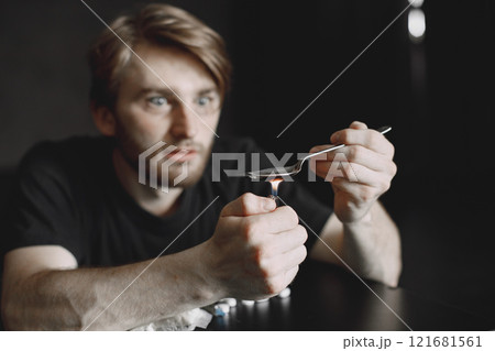 Junkie man sitting in dark room and heating spoon with heroin on lighter. Junkie man sitting in dark room and heating spoon with heroin on lighter. 121681561