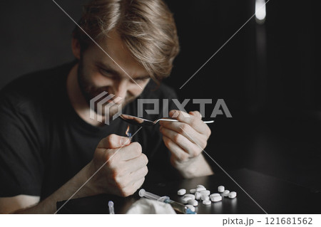 Junkie man sitting in dark room and heating spoon with heroin on lighter. Junkie man sitting in dark room and heating spoon with heroin on lighter. 121681562