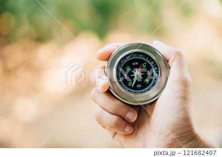 A traveler holding a compass in a park seeks guidance and direction. The compass in a woman hand set against a nature-blurred background signifies exploration and a journey to find one way. A traveler holding a compass in a park seeks guidance and direction. The compass in a woman hand set against a nature-blurred background signifies exploration and a journey to find one way. 121682407