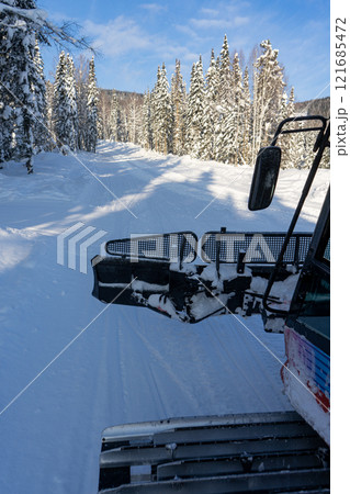A ride in the cabin of an open red snowcat, a view of the caterpillar of a snowcat on a snowy road in the forest. 121685472