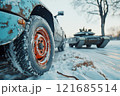 Weathered car tire in snow with military tank in the background during winter day 121685514