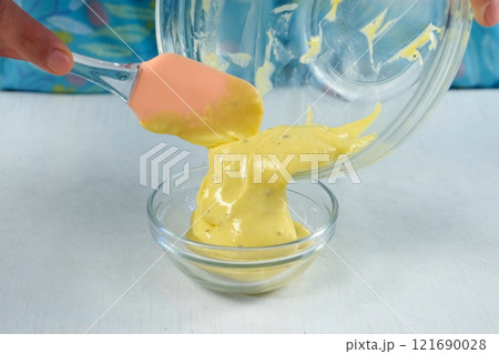 Woman preparing homemade mayonnaise putting in small glass bowl using spatula. Woman preparing homemade mayonnaise putting in small glass bowl using spatula. 121690028