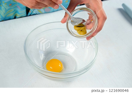 Woman cooking homemade mayonnaise adding mustard in bowl to yolk at home. 121690046