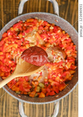 Adding a tomato paste to a pot with chopped vegetables 121690931