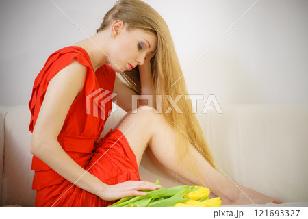 Sad elegant woman sitting on sofa with tulip Sad elegant woman sitting on sofa with tulip 121693327