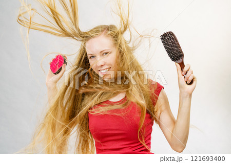 Blonde girl long blowing hair holds two brushes 121693400
