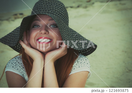 Redhaired happy girl in black hat on beach. 121693875