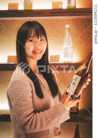 日本酒を選ぶ若い女性 【撮影協力・新潟地酒 premium SAKE 蔵KURA】 日本酒を選ぶ若い女性 【撮影協力・新潟地酒 premium SAKE 蔵KURA】 121694211