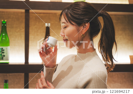 日本酒を試飲する若い女性【撮影協力・新潟地酒 premium SAKE 蔵KURA】 日本酒を試飲する若い女性【撮影協力・新潟地酒 premium SAKE 蔵KURA】 121694217