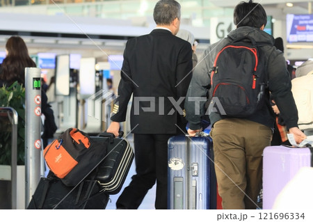搭乗ゲートに向かう乗務員と乗客 スーツケースを引く空港利用者 搭乗ゲートに向かう乗務員と乗客 スーツケースを引く空港利用者 121696334
