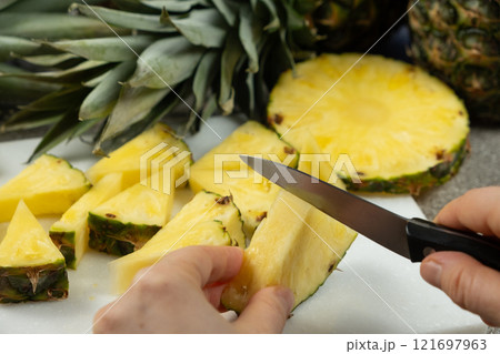 Hands cutting fresh pineapple fruit into pieces. 121697963