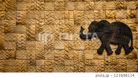 A handcrafted wooden elephant, adorned with intricate details, stands proudly against a textured, woven background of natural hues. 121698114