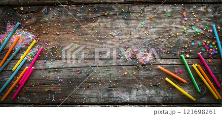 Sprinkles and colorful candy sticks are scattered across a rustic wooden table, remnants of a festive celebration and a testament to the joy of sweet treats. 121698261