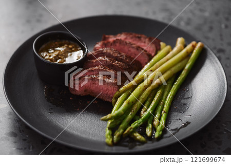 New york steak with asparagus on black plate with pesto sauce 121699674