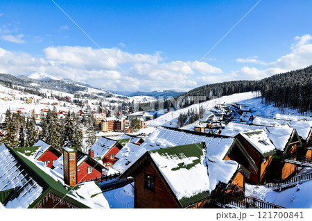 A view from above of a snow-covered winter village, harmoniously integrated into the mountain landscape. A view from above of a snow-covered winter village, harmoniously integrated into the mountain landscape. 121700841