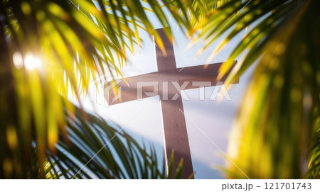 Wooden cross standing tall, surrounded by vibrant green palm leaves and sunlight filtering through, symbolizing faith and spirituality 121701743