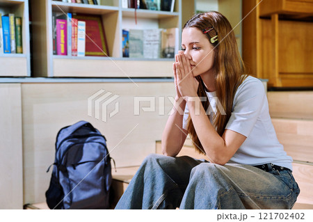 Upset sad teenage girl high school student sitting on floor in library classroom 121702402