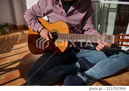Man playing acoustic guitar while sitting on a sunlit tiled floor Man playing acoustic guitar while sitting on a sunlit tiled floor 121702966