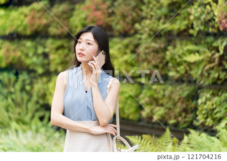 壁面緑化されたビルの前でスマートフォン(スマホ)で電話するビジネスウーマン 壁面緑化されたビルの前でスマートフォン(スマホ)で電話するビジネスウーマン 121704216