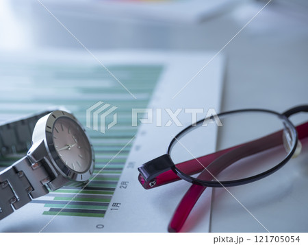 テーブルに置かれたグラフとメガネと腕時計 121705054
