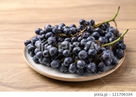 Black grapes on plate with wooden table, Seedless grapes Black grapes on plate with wooden table, Seedless grapes 121706384