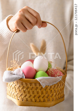 White easter eggs with bunny rabbit ears and colorful easter eggs in basket holding by hand 121706417