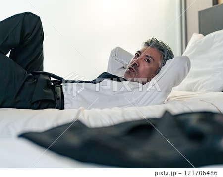 スーツを着たままベッドに寝転がるミドル男性ビジネスパーソン スーツを着たままベッドに寝転がるミドル男性ビジネスパーソン 121706486